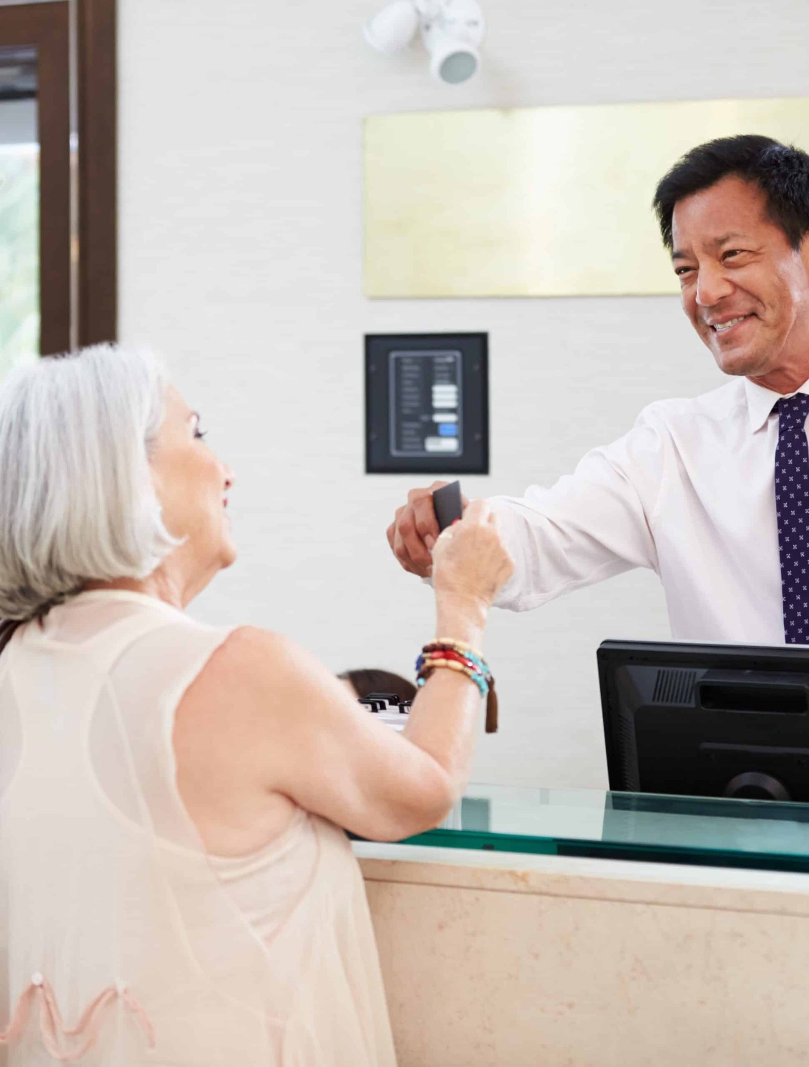 Senior Couple Checking In At Hotel Reception - Nohée