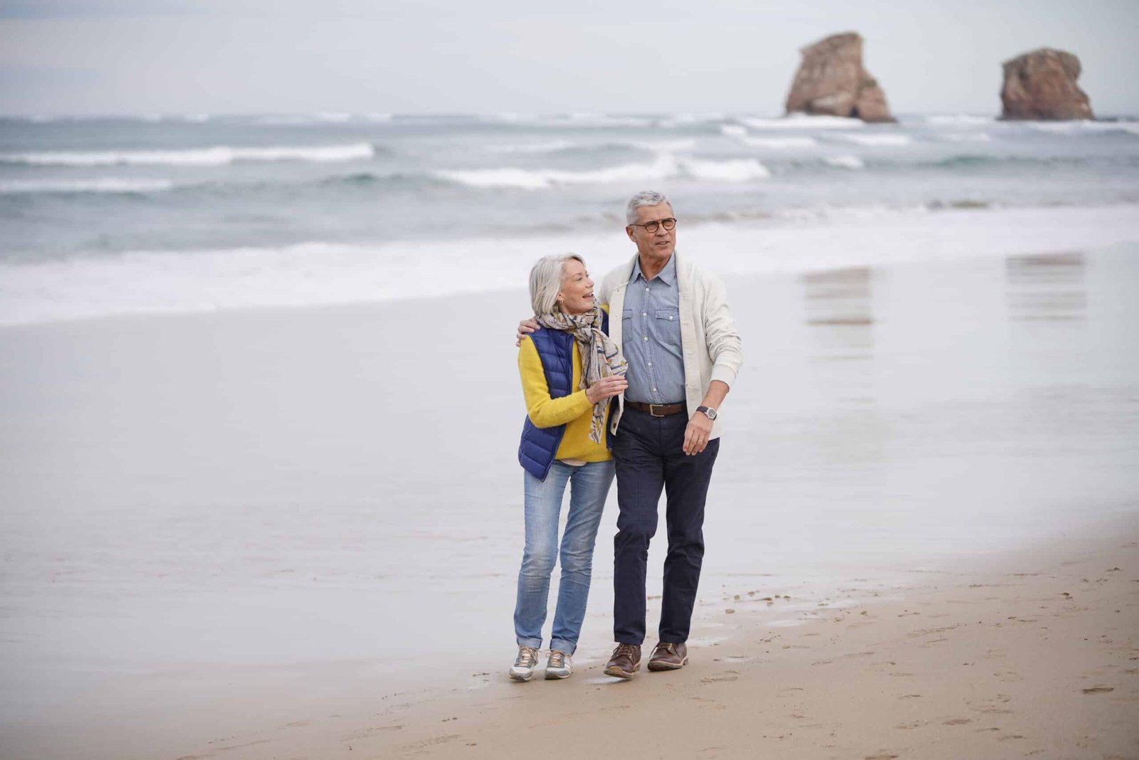 Happy senior couple walking together on the beach - Nohée