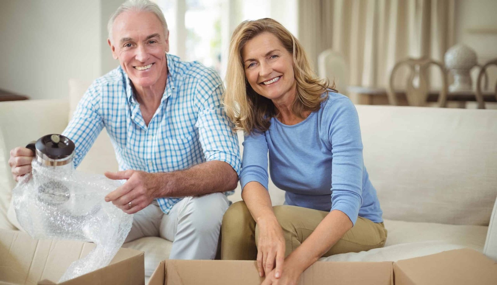 Smiling senior couple unpacking carton boxes in living room - Nohée