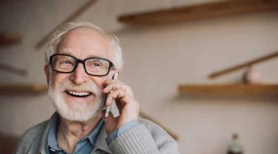 Homme senior souriant parlant au téléphone pour aide pour maison de retraite dans un intérieur chaleureux